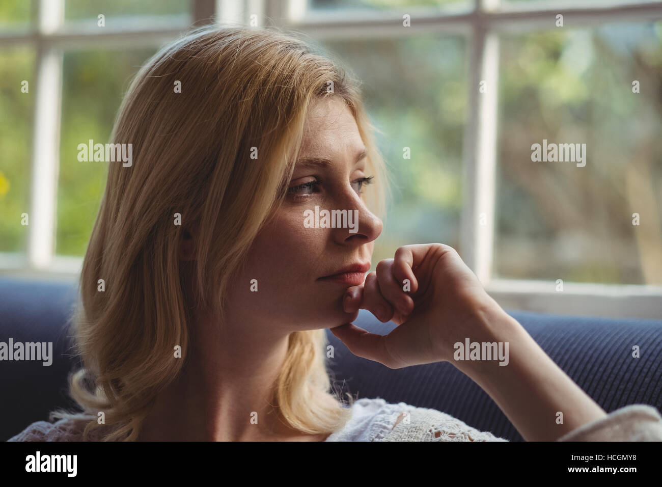 Nachdenkliche Frau Blick durch Fenster im Wohnzimmer Stockfoto
