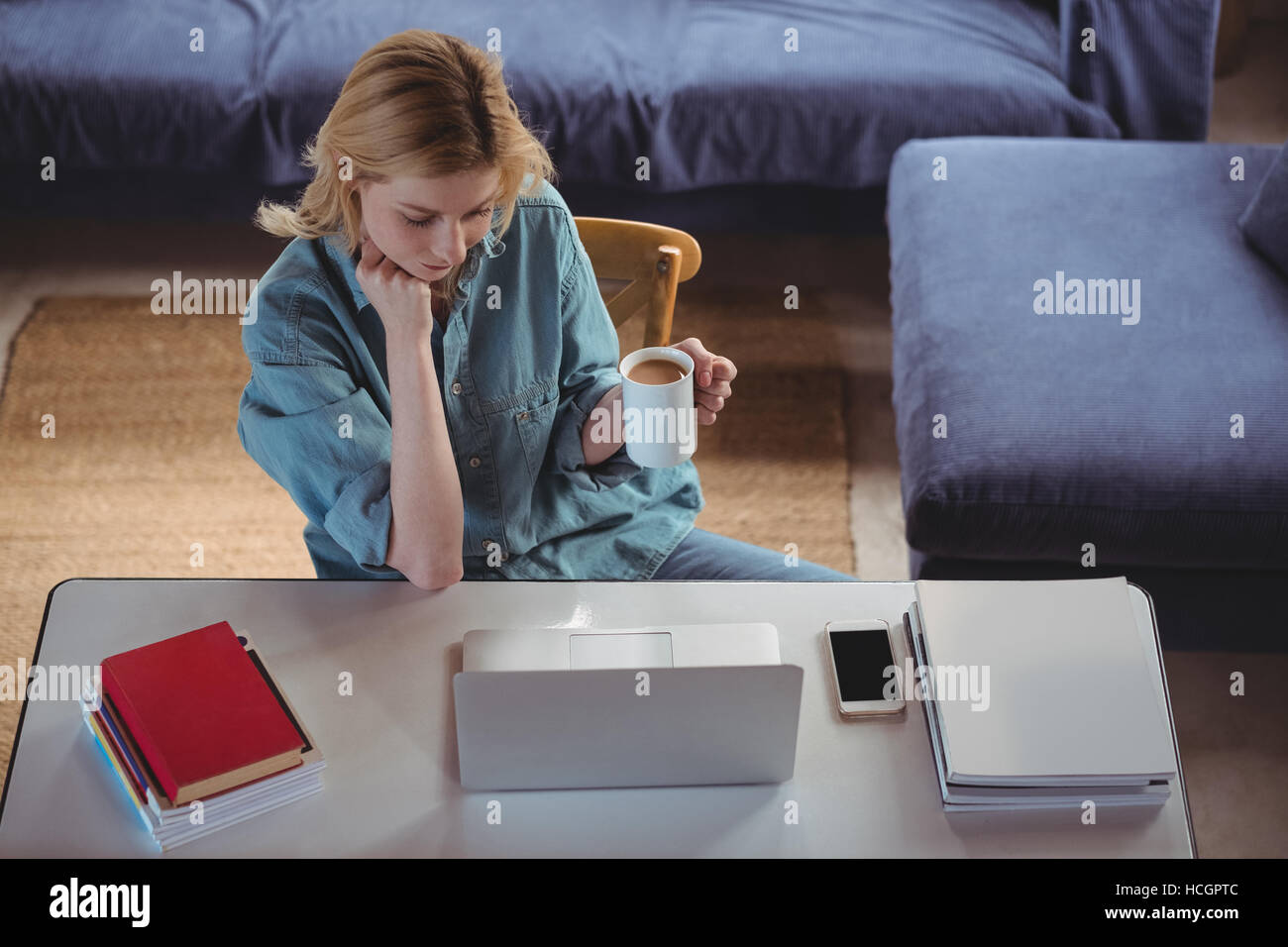 Schöne Frau mit Kaffee während mit Laptop im Wohnzimmer Stockfoto