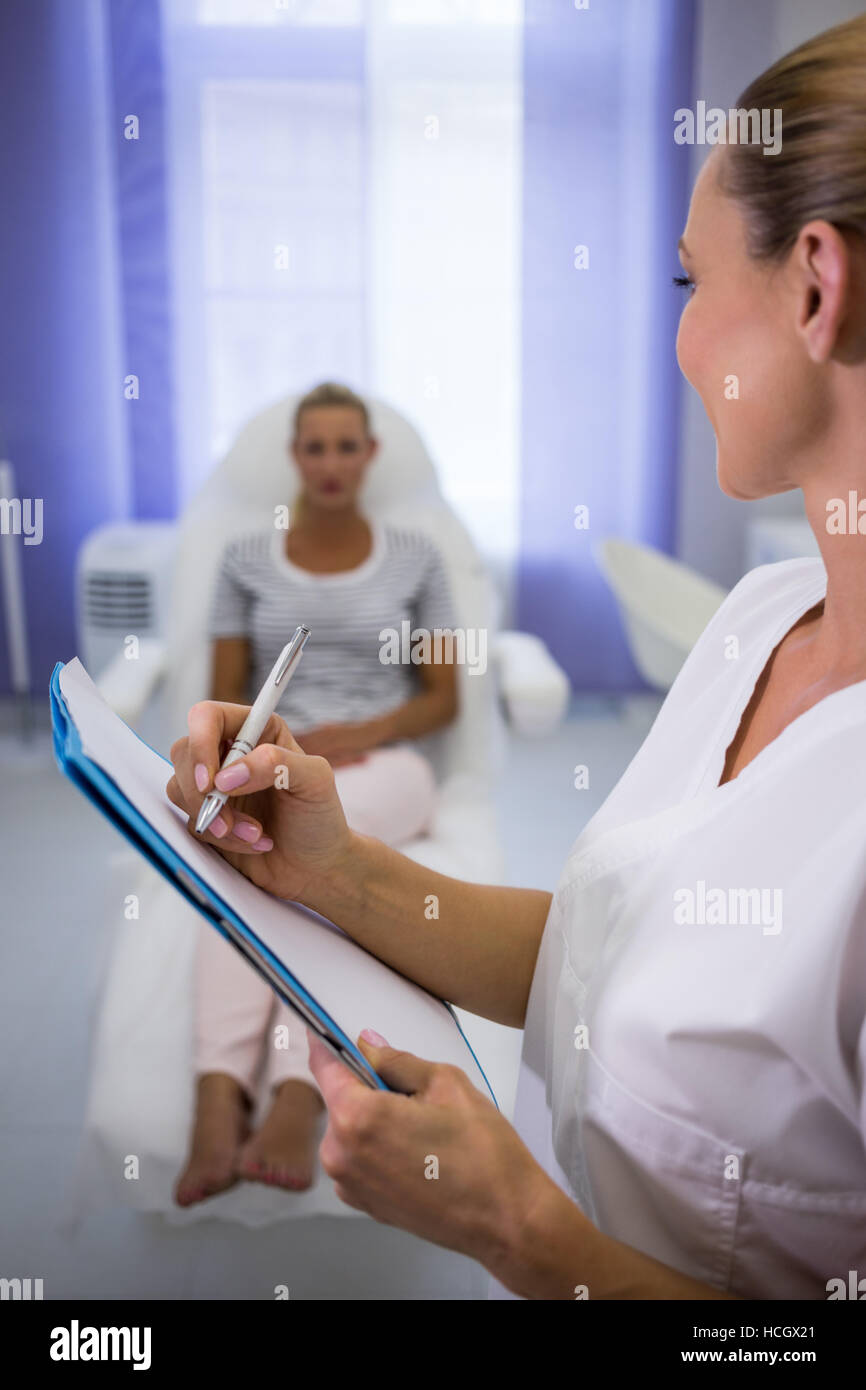 Arzt, medizinische Berichte zu schreiben, während im Gespräch mit Patienten Stockfoto