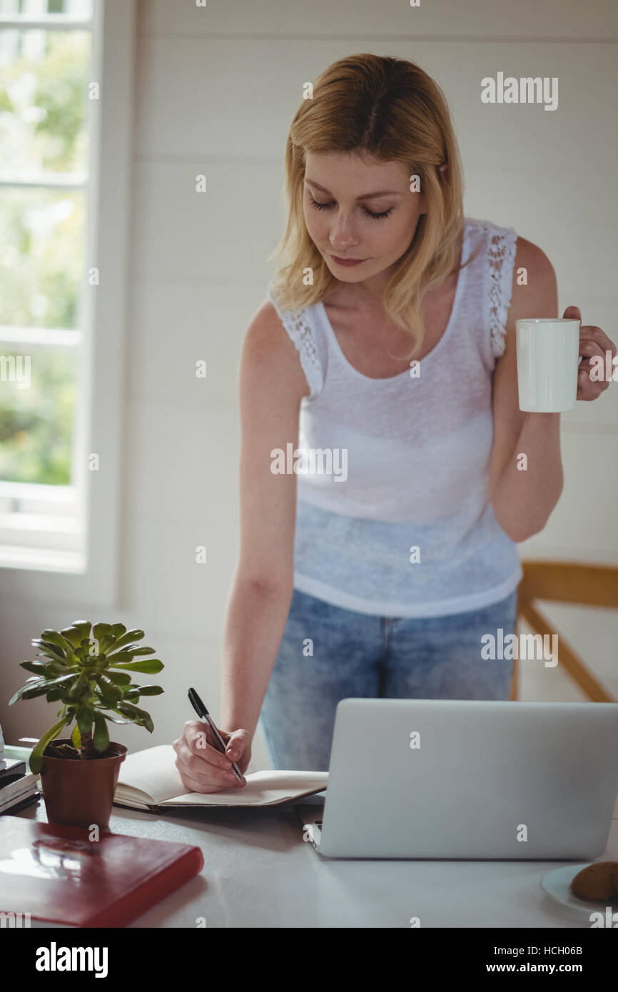 Schöne Frau in Tagebuch zu schreiben, während mit Kaffee im Wohnzimmer Stockfoto