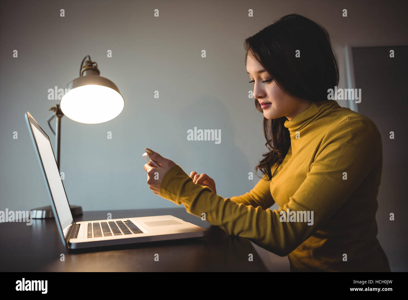 Frau mit Handy während der Arbeit am Laptop im Arbeitszimmer Stockfoto