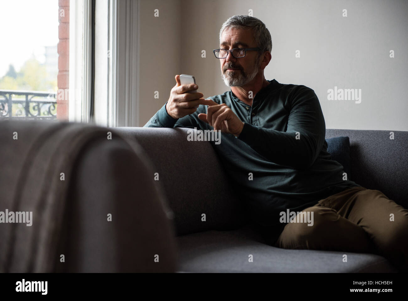 Mann mit Handy im Wohnzimmer Stockfoto