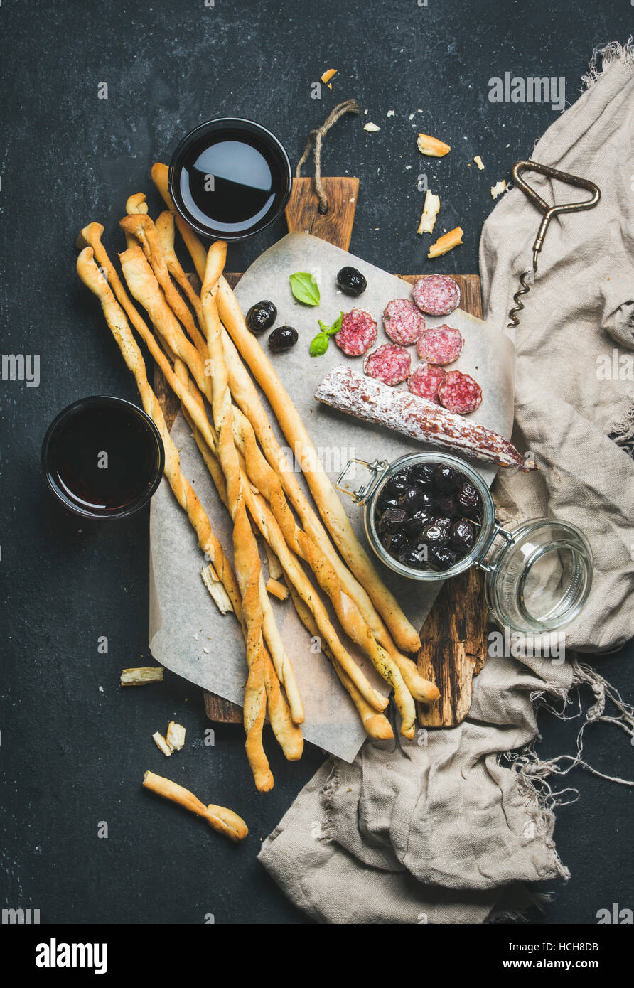 Wein und Häppchen festgelegt. Italienische Grissini Brot-Sticks, trockenen Wurstwaren Fleischwurst, schwarzen Oliven auf rustikalen hölzernen Portion Board und Rotwein im Glas Stockfoto