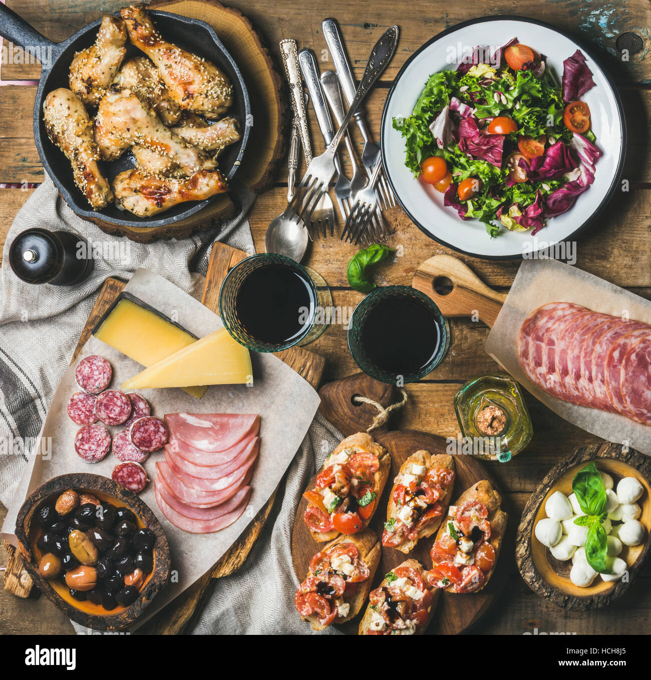 Hause Abendessen Partei Tischgesteck. Rustikalen Tisch set mit Salat, Oliven, Huhn, Tomaten, Feta Käse Brushettas, Snacks und Rotwein, Ansicht von oben. SLO Stockfoto