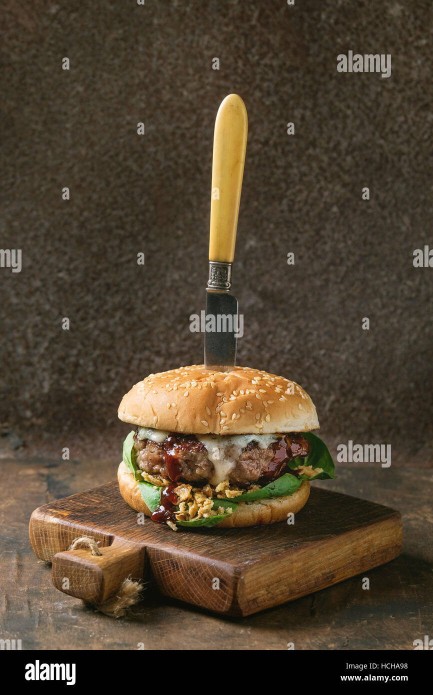 Hamburger mit Rindfleisch-Burger-Schnitzel, gebratenen Zwiebeln, Spinat, Ketchup-Sauce und Blauschimmelkäse in traditionellen Brötchen serviert auf Holz Schneidebrett mit Jahrgang Stockfoto