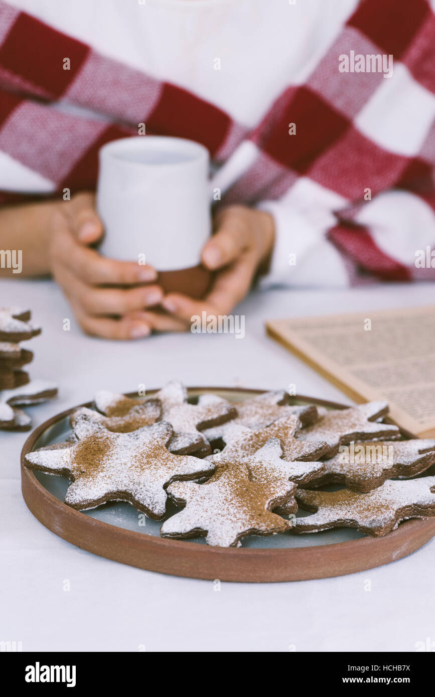 Eine Frau, die Kaffee und Schneeflocke Cookies beim Lesen eines Buches. Stockfoto