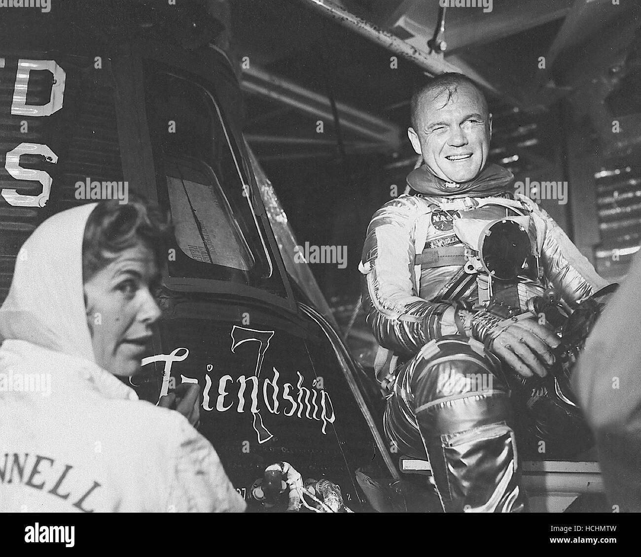 Astronaut John H. Glenn Jr., Pilot der Mission Mercury-Atlas 6 "Friendship 7" ist geeignet und sitzt neben seiner Kapsel während der Pre-Flight-Aktivität in Cape Canaveral. Glenn ist mit der Künstlerin Cecilia Bibby gezeigt, die den Namen "Friendship 7" auf seinem Mercury-Raumschiff gemalt. Credit: NASA über CNP /MediaPunch Stockfoto