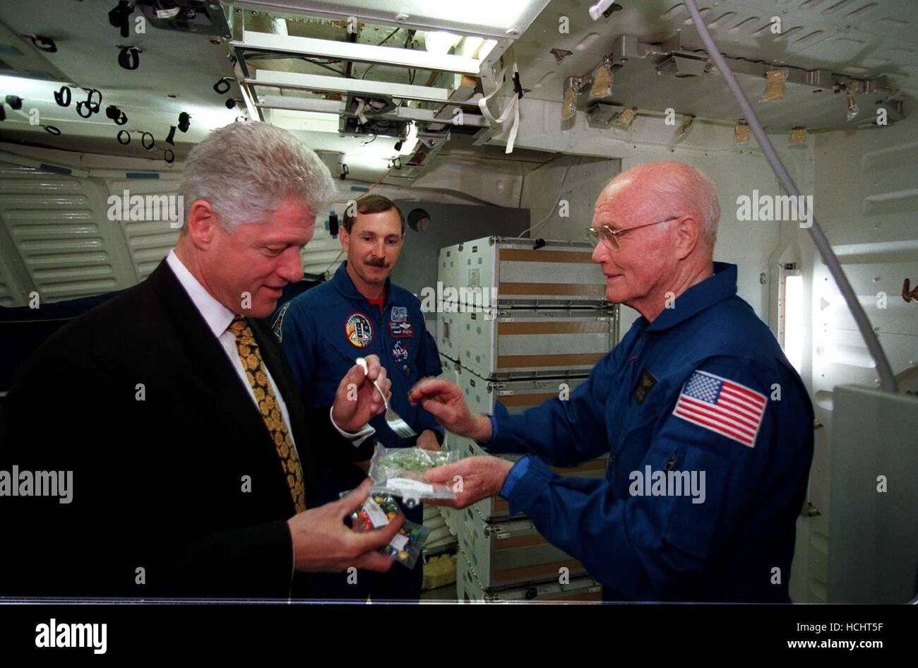 US-Präsident Bill Clinton bereitet sich auf eine Gabel benutzen, um etwas Platz zu Essen probieren Sie während des Besuchs der NASA Johnson Space Center (JSC) am 14. April 1998. Halten, dass das Essen Paket ist US-Senator John H. Glenn Jr. (Demokrat of Ohio), geplant derzeit in Ausbildung bei JSC als Nutzlastspezialisten für einen Flug noch in diesem Jahr an Bord der Raumfähre Discovery. Mit Blick auf ist Astronaut Curtis L. Brown Jr., Kommandant von STS-95. Das Bild wurde in der volle Rumpf-Trainer (FFT) aufgenommen. . Bildnachweis: Joe McNally, National Geographic für die NASA über CNP - kein Draht-SERVICE - Foto: Joe Mcnally, National Geographic Stockfoto