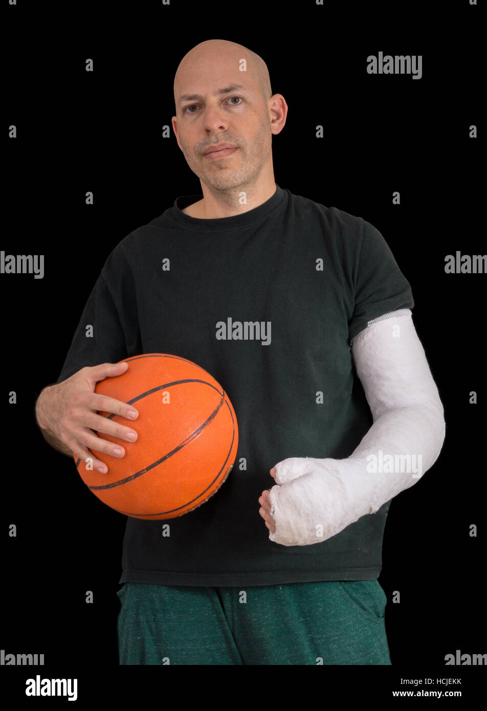 Junger Mann Sport eine helle weiße Gipsarm, hält einen Basketball nach dem Bruch seines Handgelenks bei einem Basketball-Spiel Sturz, isoliert auf schwarz Stockfoto