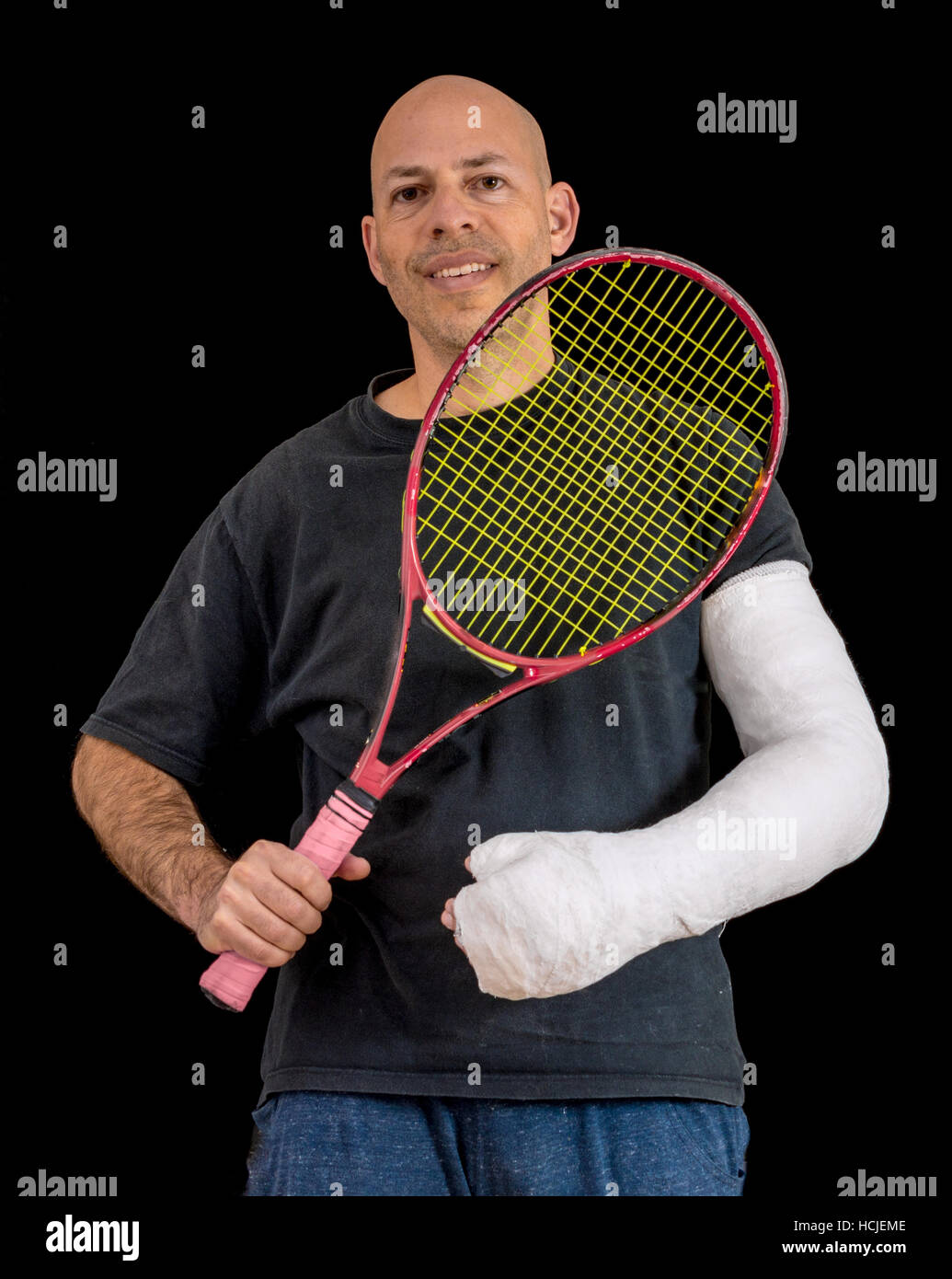 Junger Mann hält einen Tennisschläger nach seinem Handgelenk zu brechen, in einem Tennis-Spiel, eine helle weiße sportliche arm Cast, isoliert auf schwarz Stockfoto