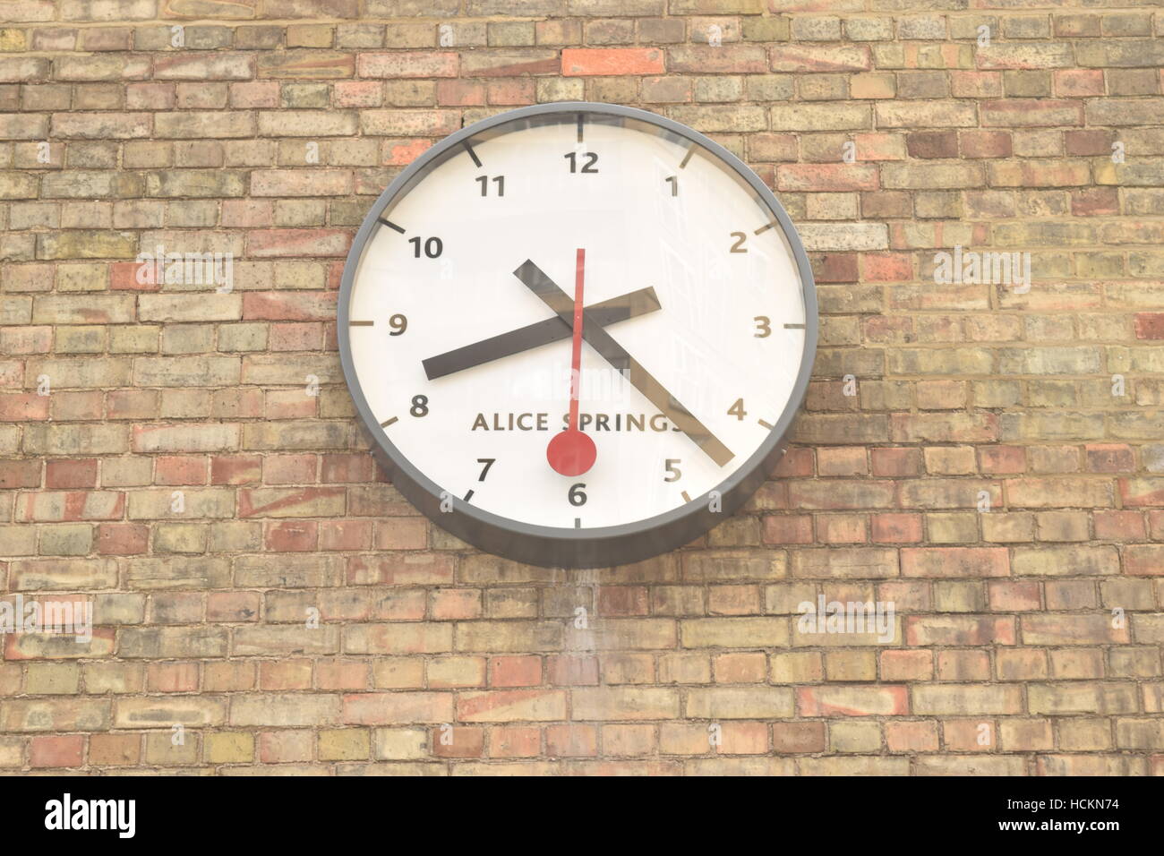 Weiße Uhr auf eine Mauer mit schwarzen und roten Händen am Kings Cross St Pancras Stockfoto