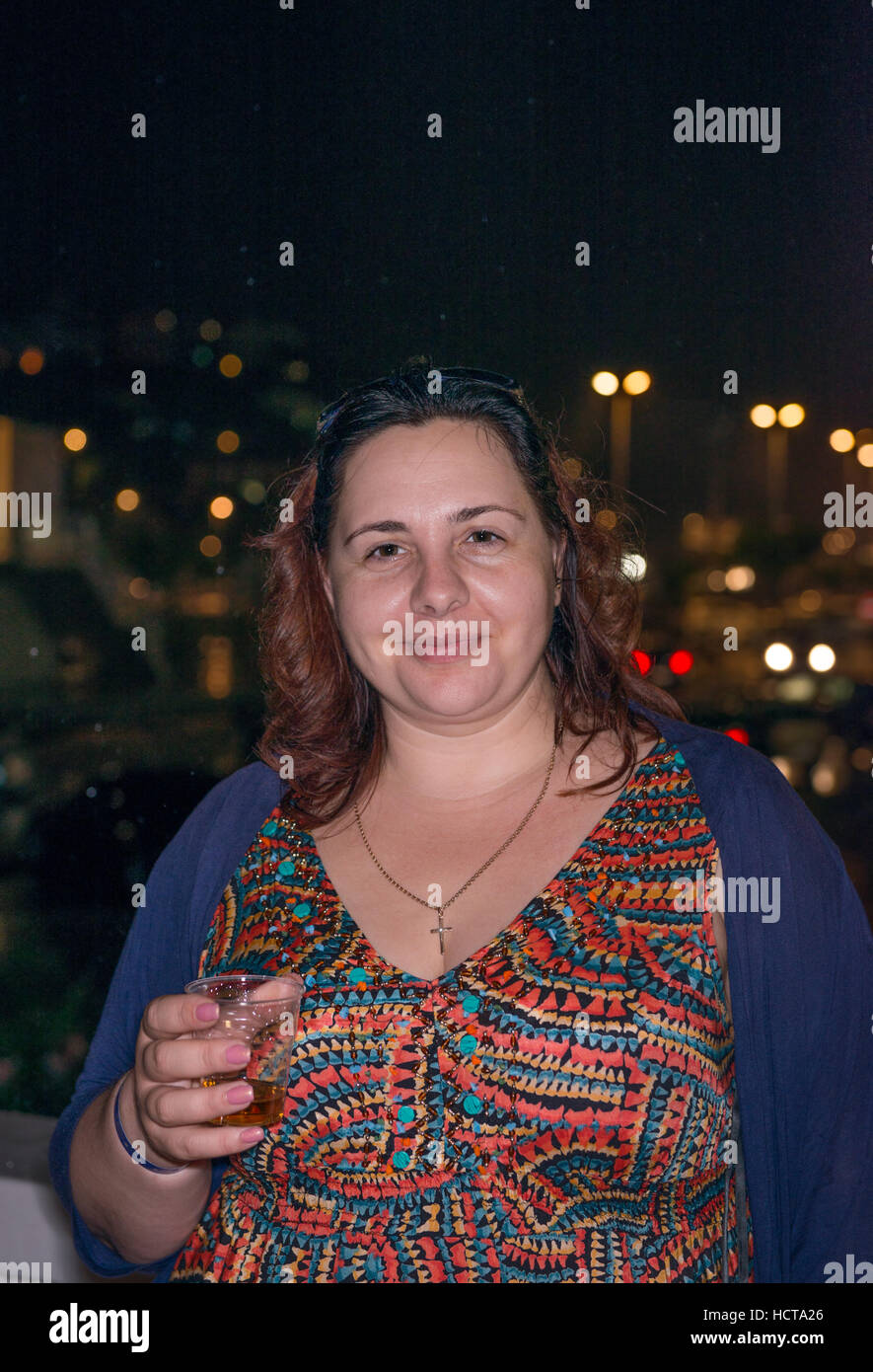 Brustbild der Reife dicke Frau, die mit Kunststoff-Kappe in der Hand auf Nacht Lichter Hintergrund steht. Stockfoto