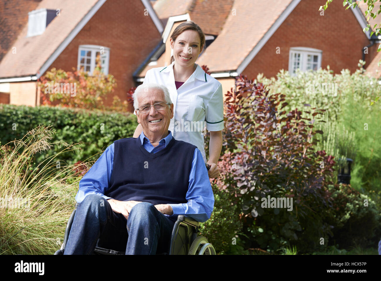 Pflegeperson Senior Mann im Rollstuhl schieben Stockfoto