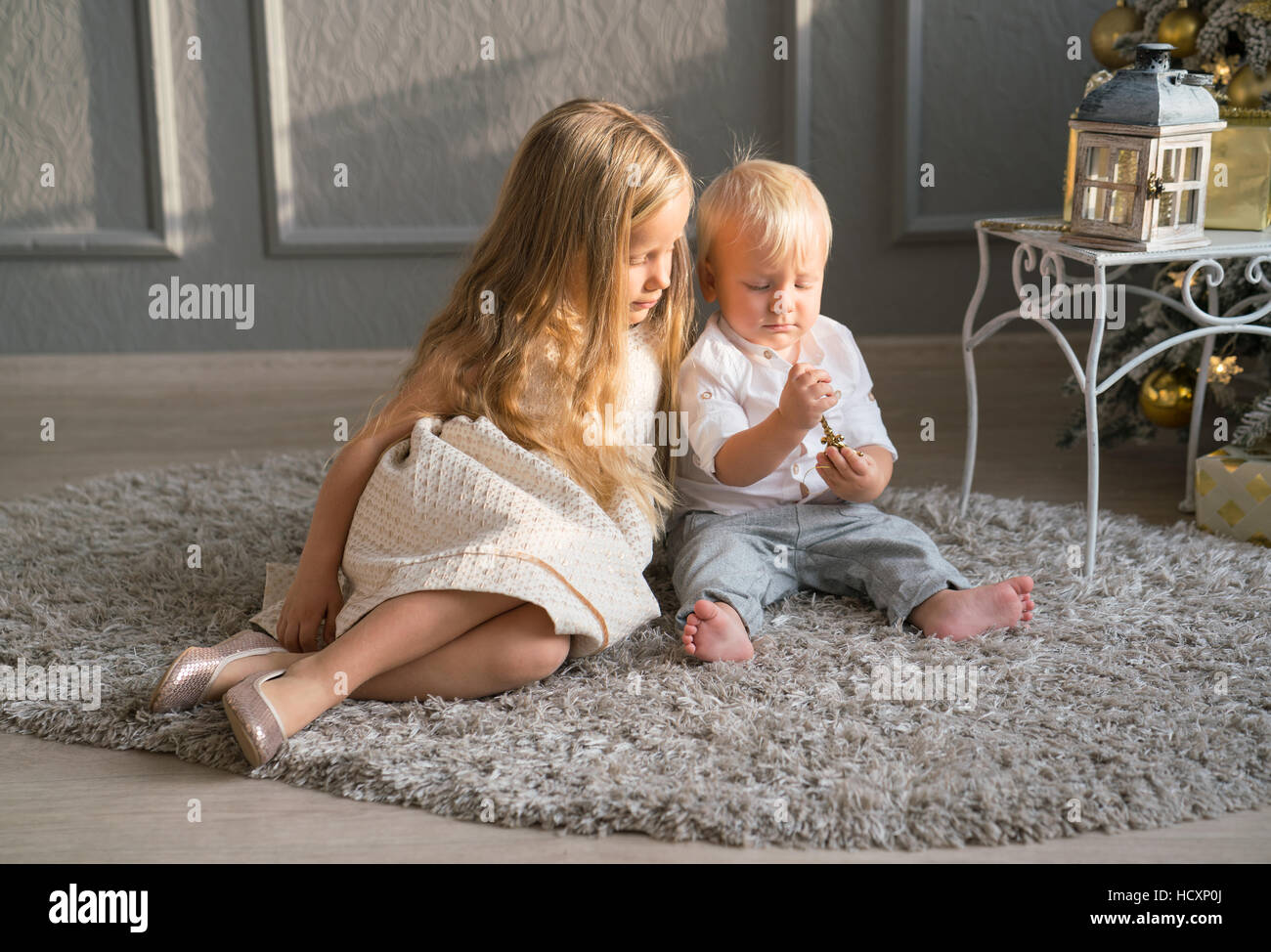 Niedliche Kinder spielen zusammen in der Nähe von Weihnachtsbaum im Innenbereich. Stockfoto