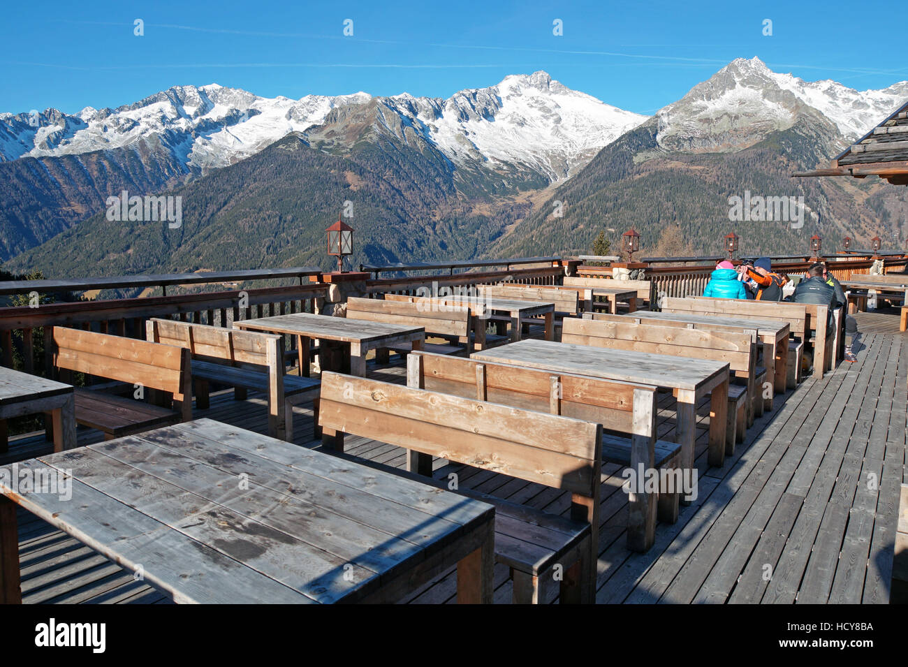 Outdoor-Restaurant in den Bergen Image mit der Terrasse, umgeben von den Alpen, das rustikale hölzerne Tische bereit, die Gäste zu empfangen. Stockfoto