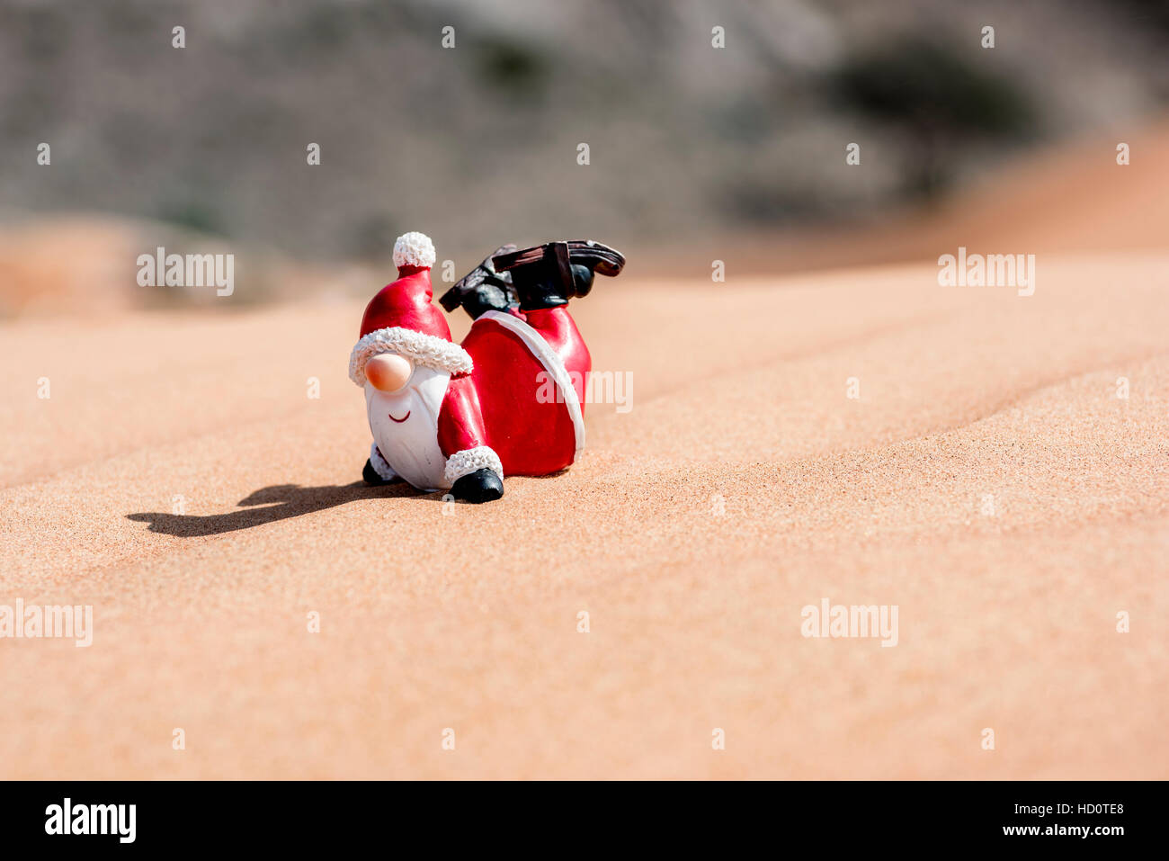 Lustige Weihnachtsmann-Figur, die in der Wüste auf dem Sand zu rutschen scheint Stockfoto