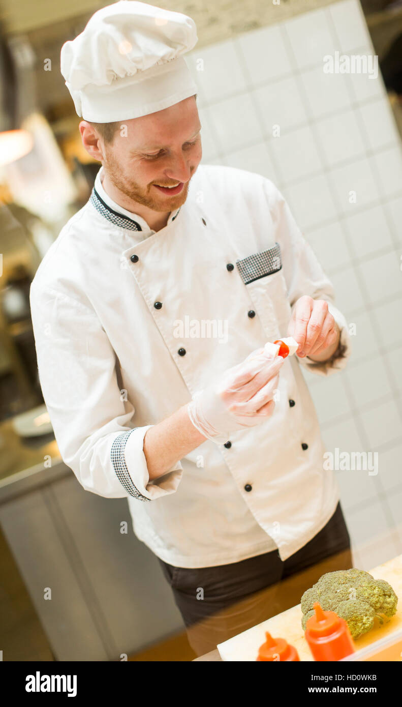 Jungkoch mit weißen Uniform steht eine moderne Küche im Restaurant und Zubereitung von Speisen Stockfoto