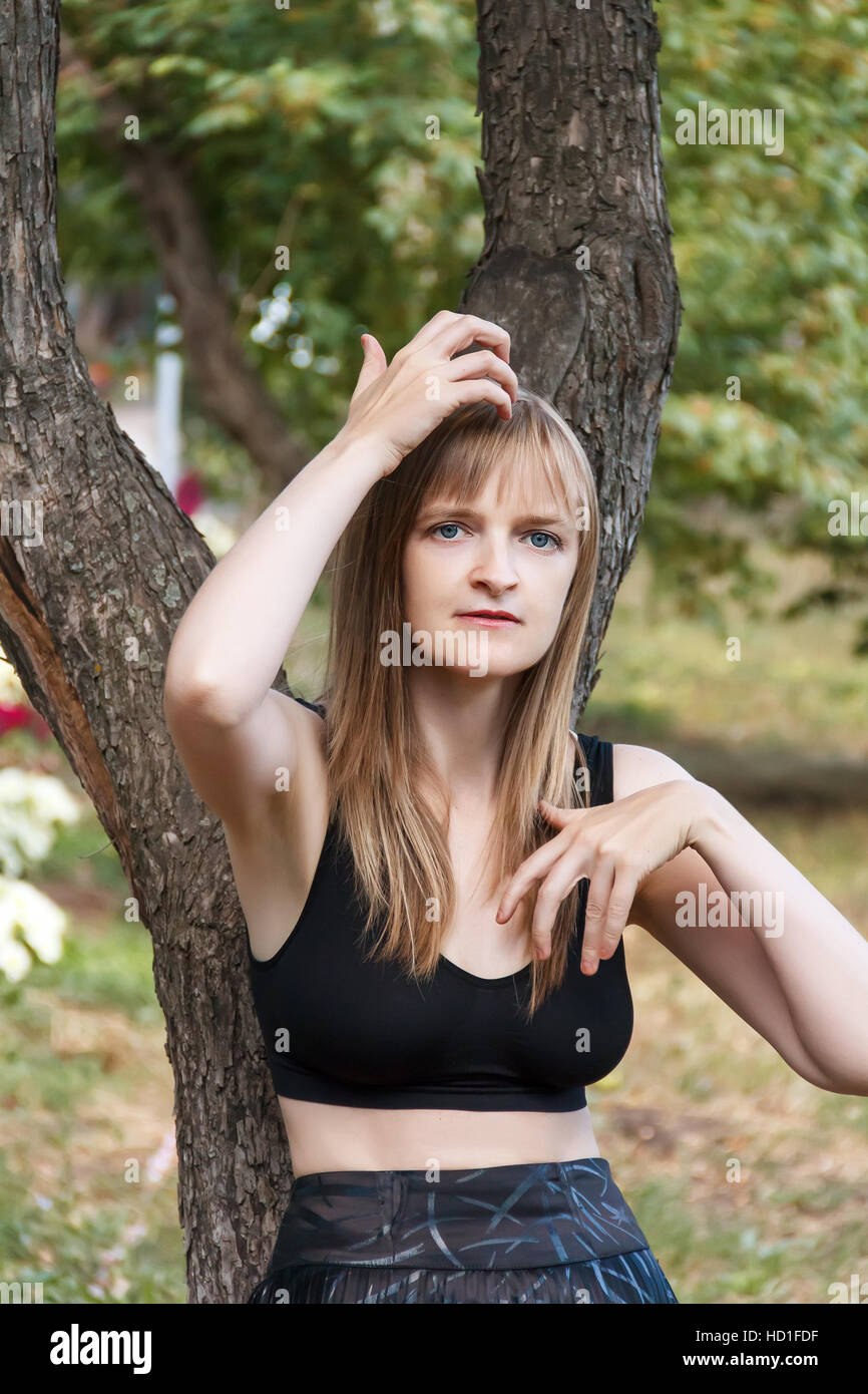 Blonde Frau, die Korrektur der Frisur in der Nähe von Baum im Sommer Stockfoto
