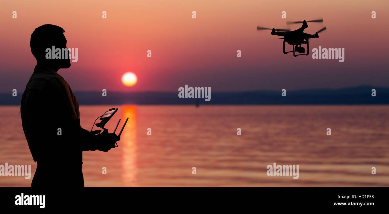 Mann eine Drohne in der Nähe von Meer in den Sonnenuntergang fliegen. Stockfoto