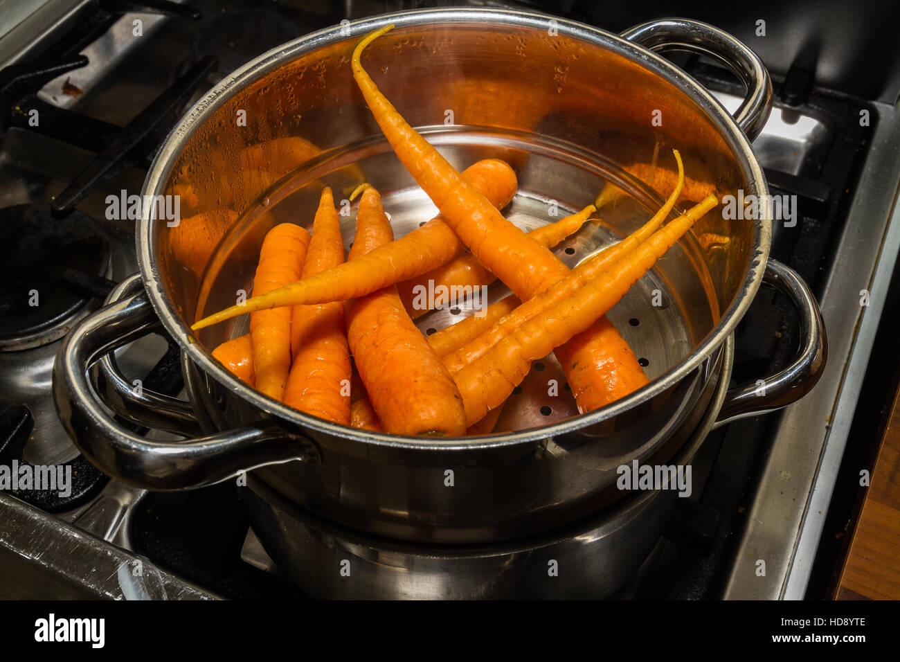 Karotten oder Daucus Carota in einem Edelstahl-Dampfer auf einem Kochfeld gedämpft wird. Stockfoto