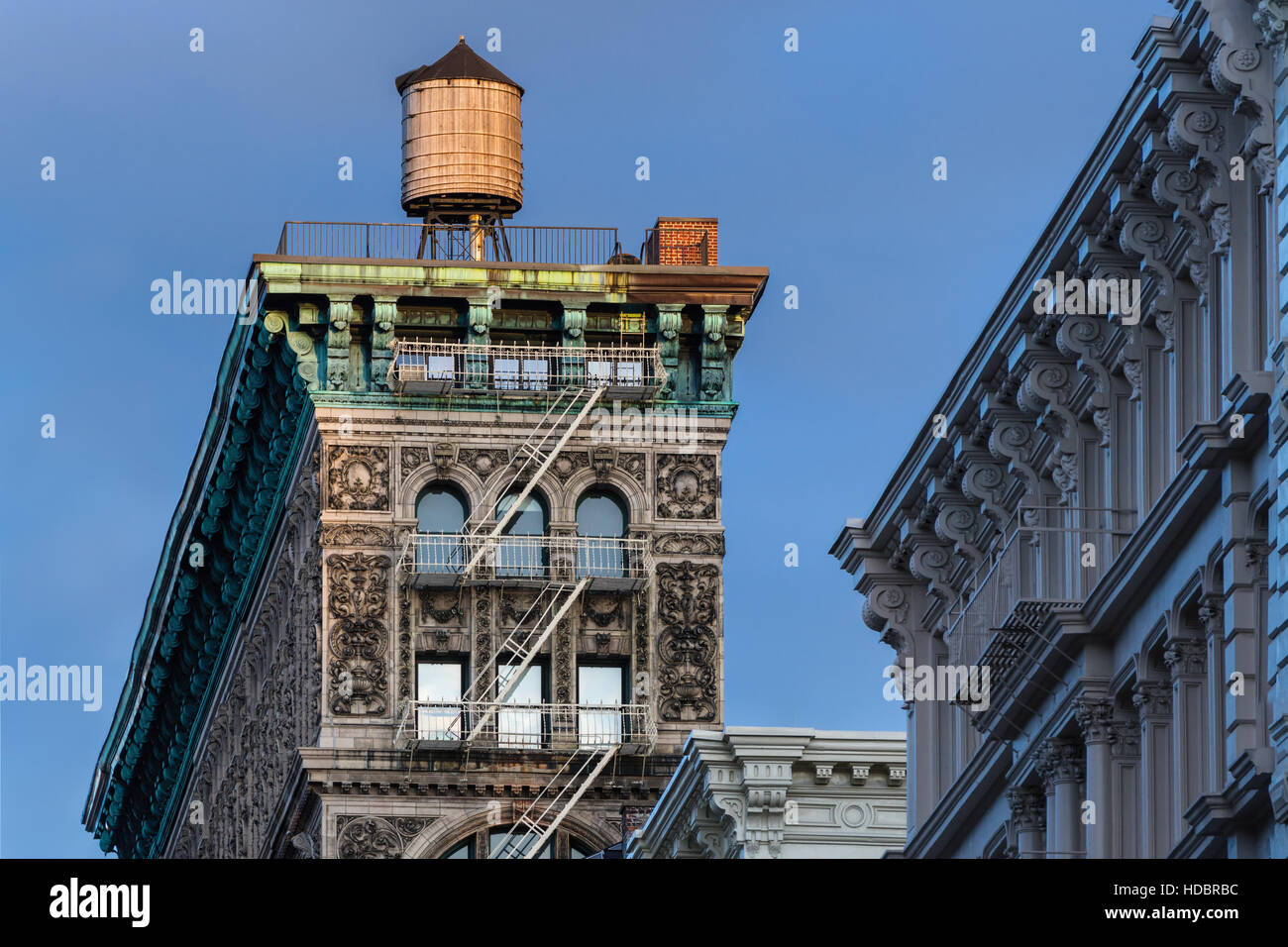 Soho-Gebäude mit Terra Cotta Verzierung, Gesims, Feuerleiter und Wasserturm von Abendlicht beleuchtet. New York City Stockfoto