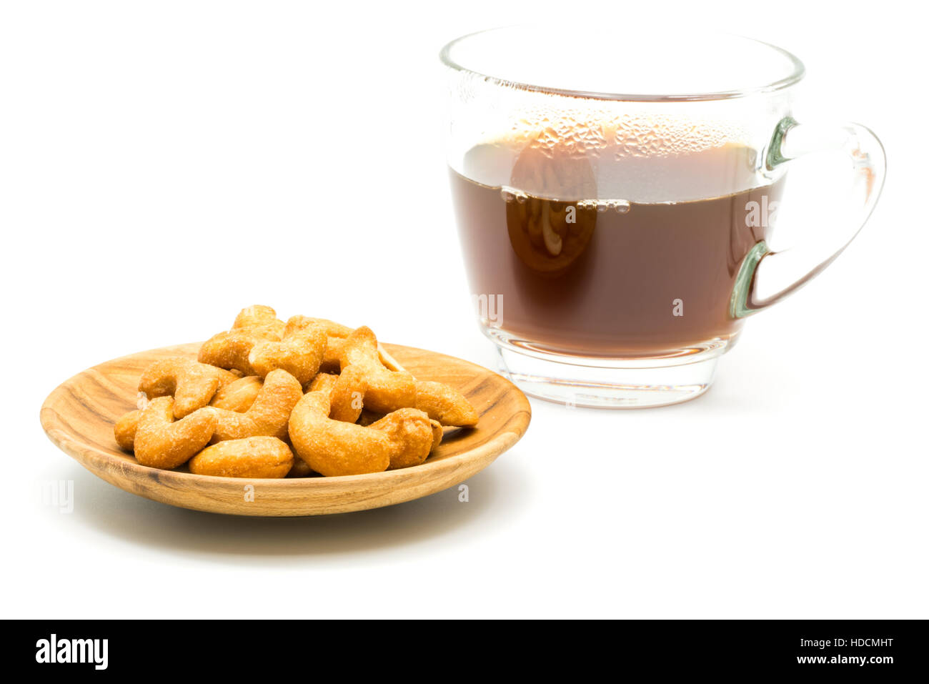 Salzige Cashew-Nüssen in Holzplatte und eine Tasse Kaffee auf weißem Hintergrund Stockfoto