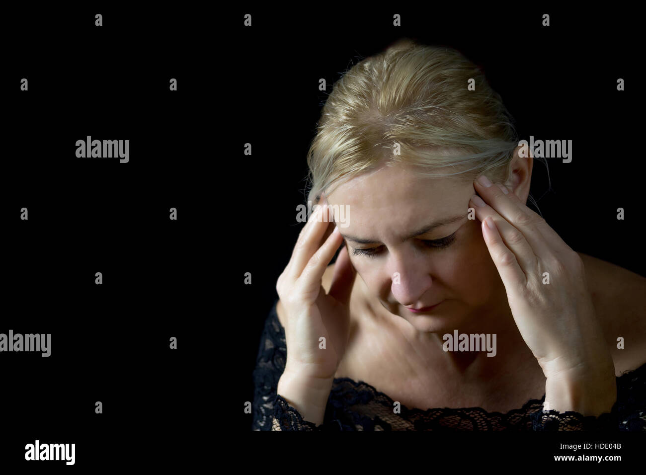 Niedrige wichtige Porträt unglücklich blonden mittlere gealterte Frau unterstützen den Kopf mit den Händen. Alles ist auf einem schwarzen Hintergrund. Stockfoto