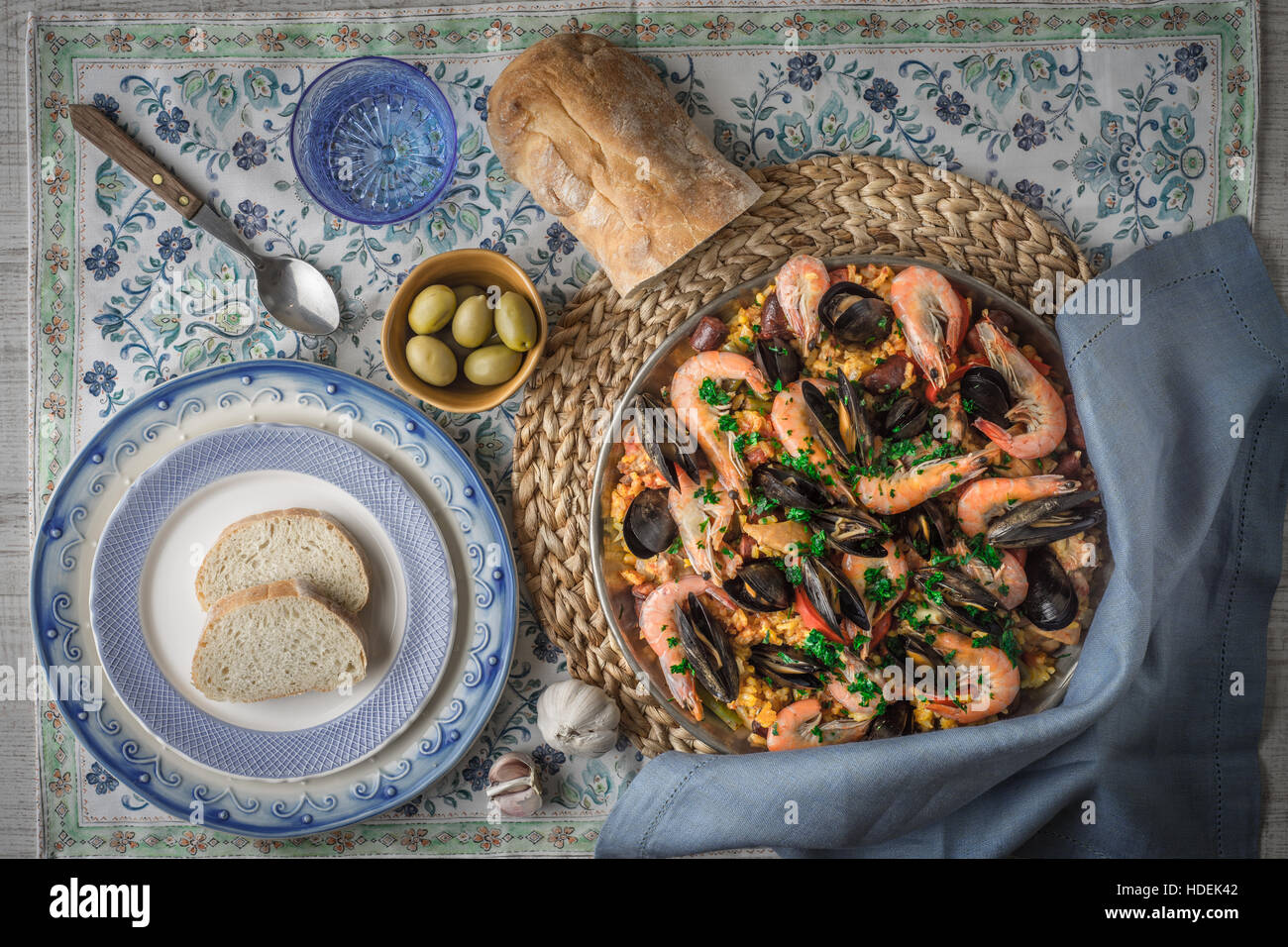 Paella auf der Metallplatte auf die schöne Serviette mit Geschirr und Brot Draufsicht Stockfoto