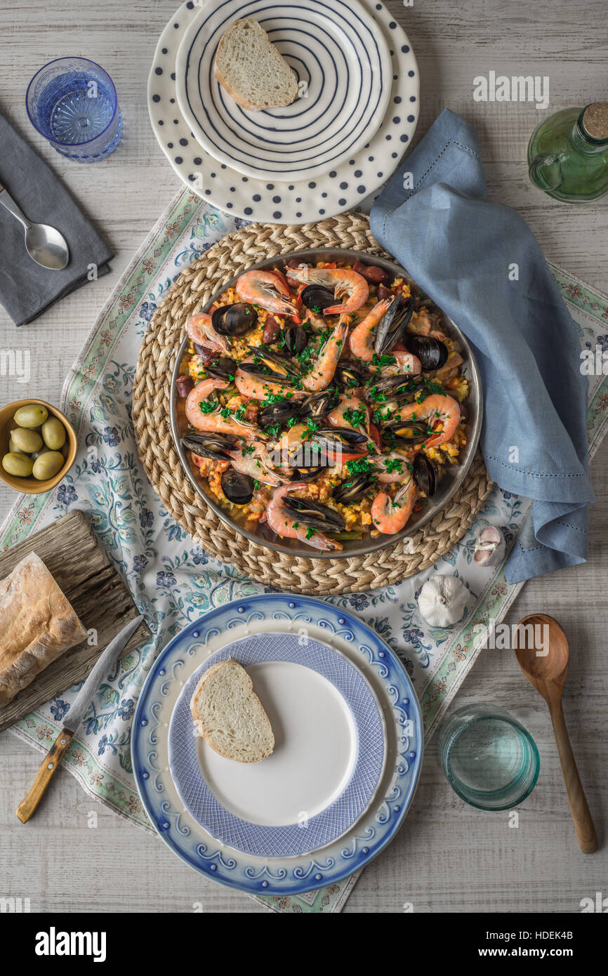 Paella auf der Metallplatte auf die schöne Serviette mit Geschirr und Brot vertikale Stockfoto