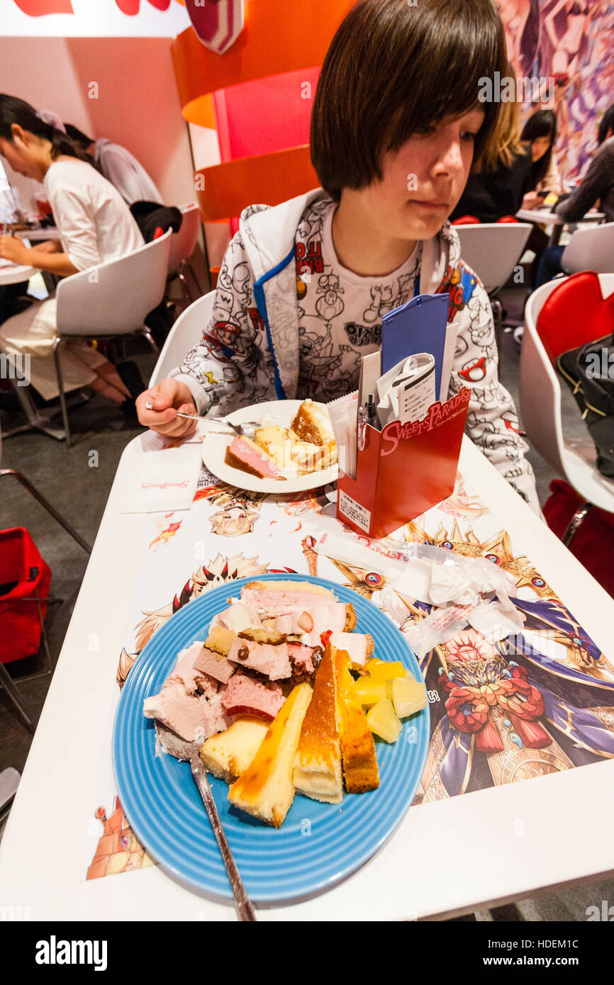 Japan. Kaukasier Kind, Teenager, 13 Jahre alt, am Tisch sitzend mit Teller voll von Kuchen im "Paradies", ein All-you-can-beliebten Kuchen Kette essen. Stockfoto