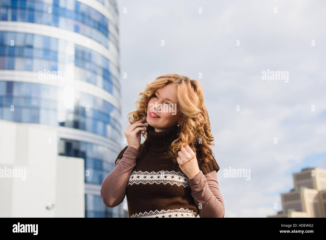 Mädchen posiert auf dem Dach des Einkaufszentrums. Stadt, modernes Gebäude im Hintergrund. Mädchen, gekleidet in braunen Pullover mit einer Christbaumkugel. Stockfoto