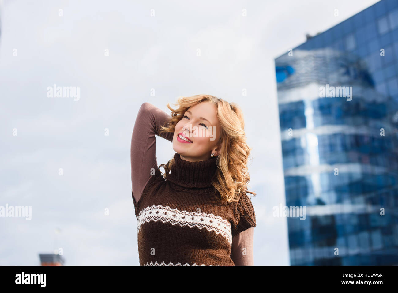 Mädchen posiert auf dem Dach des Einkaufszentrums. Stadt, modernes Gebäude im Hintergrund. Mädchen, gekleidet in braunen Pullover mit einer Christbaumkugel. Stockfoto