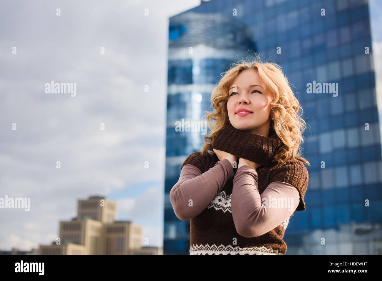 Mädchen posiert auf dem Dach des Einkaufszentrums. Stadt, modernes Gebäude im Hintergrund. Mädchen, gekleidet in braunen Pullover mit einer Christbaumkugel. Stockfoto