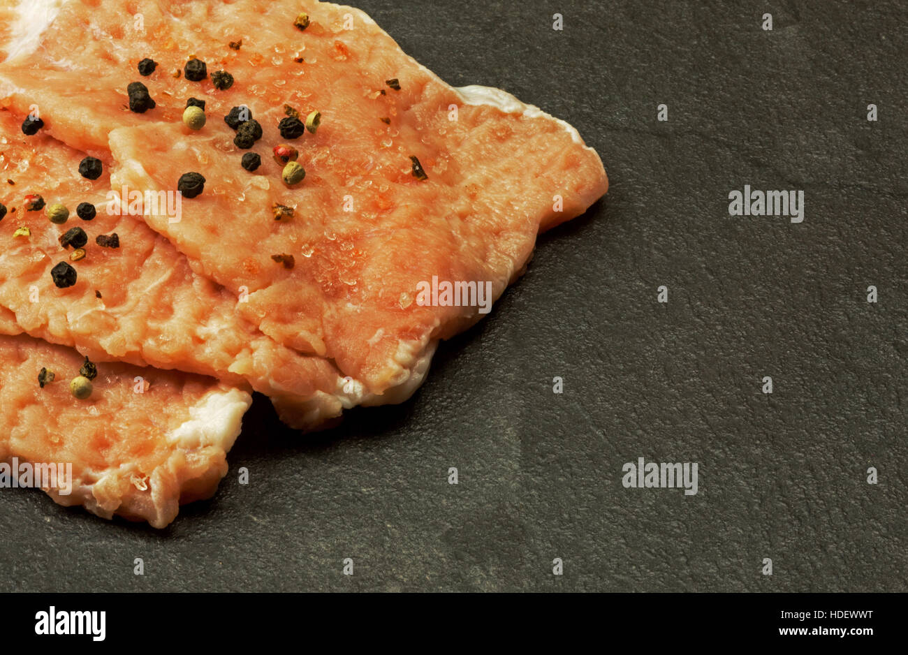 Drei Stücke von rohem Fleisch auf dem Kotelett Schnitzel mit Pfefferkörnern und Salzkristalle auf alten steinernen Küchentisch bestreut. Flache, horizontale Ansicht schließen Stockfoto