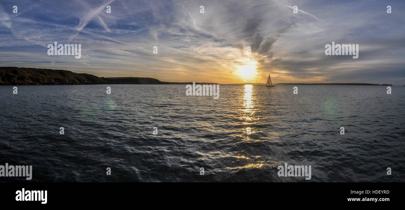 Ein Segelboot genießt den Moment, als eine goldgelbe Sonne über dem Wasser. Stockfoto