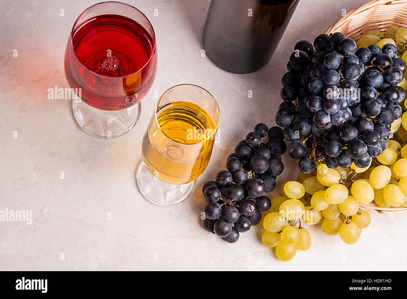 Zwei Gläser - eine mit Weißwein und eine mit roten Wein und braune Flasche mit Weißwein auf hellen Marmor Hintergrund. Stockfoto