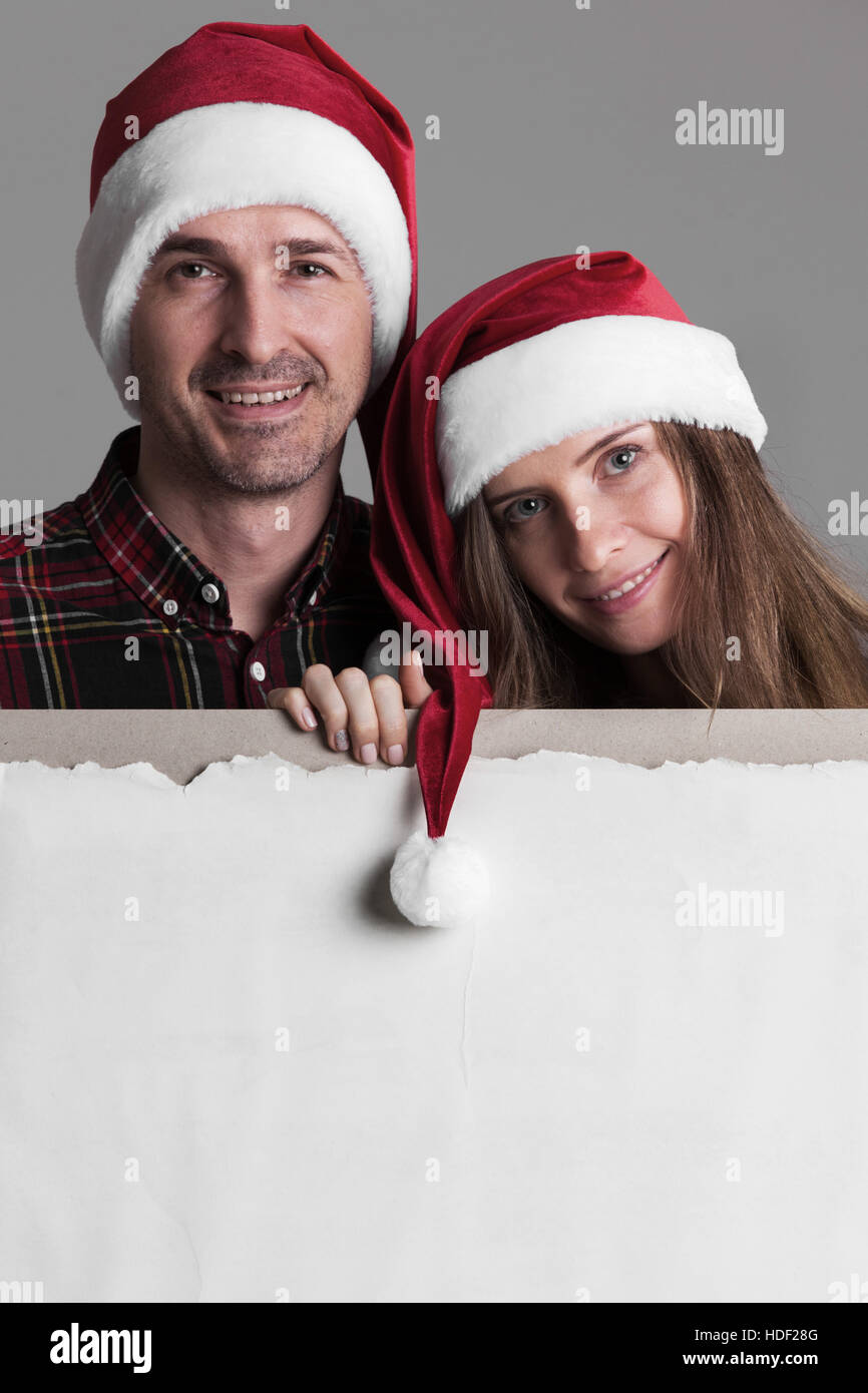 Glücklich lächelnd paar in Santas Hüte mit weißen leeren Banner mit Textfreiraum Stockfoto