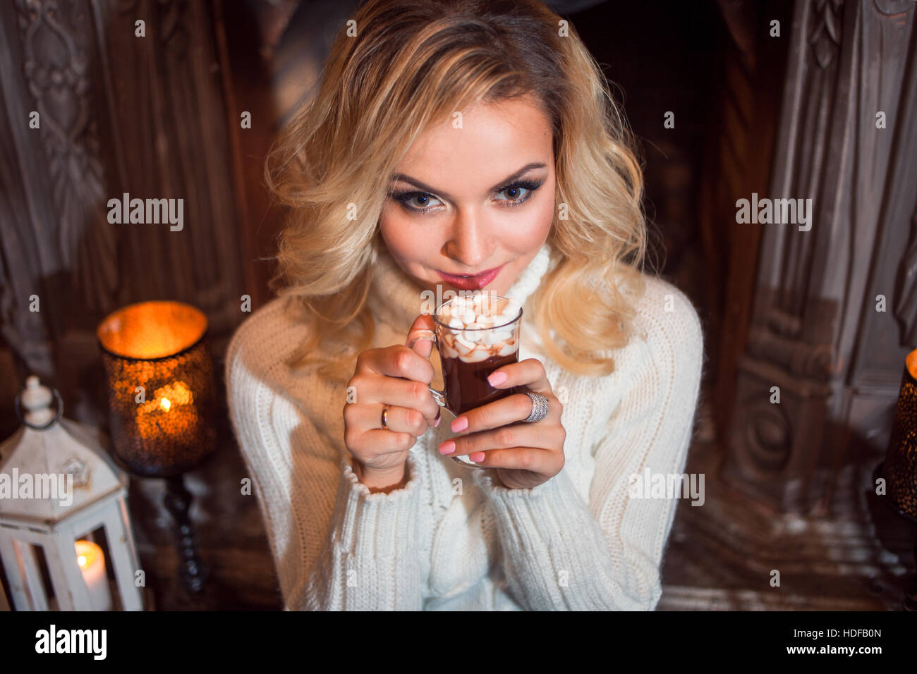 Junge Frau gekleidet herzlich, trinken heißen Schokolade in der Nähe von Kamin sitzen Stockfoto