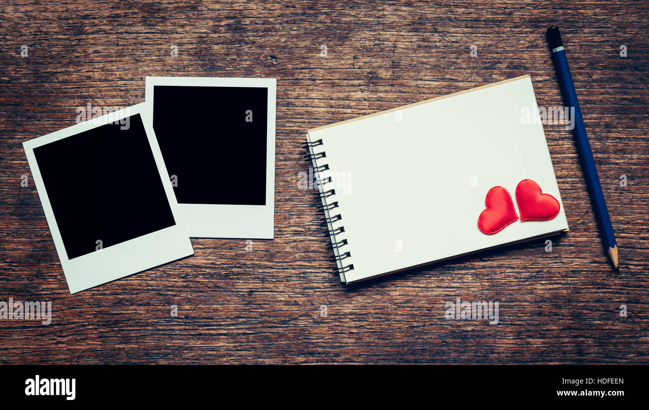 Leere Foto Frame, Notebook, Bleistift und Rot Herz zum Valentinstag auf Holztisch Hintergrund. Stockfoto