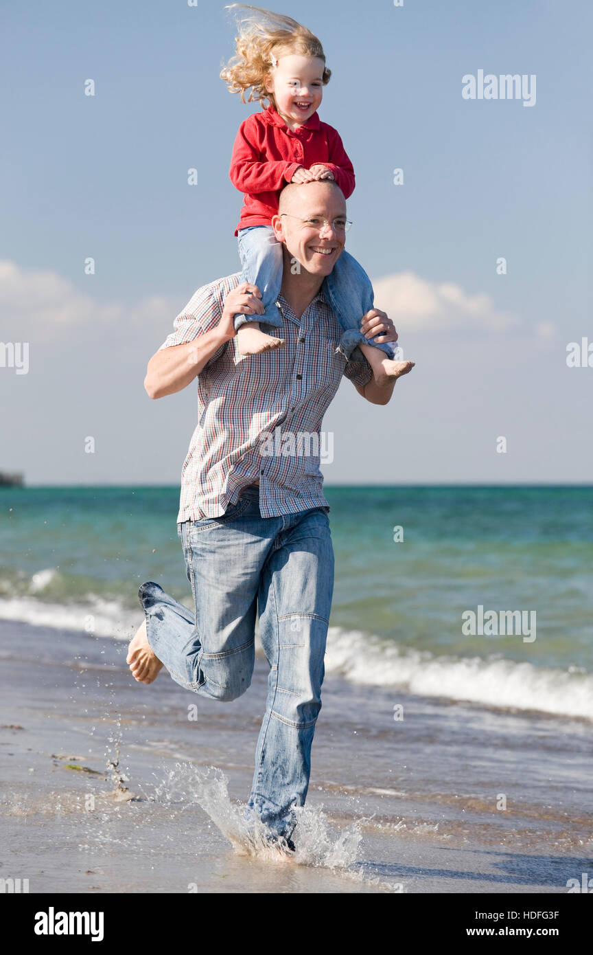 Glücklicher Vater seine Tochter auf seinen Schultern am Strand tragen Stockfoto