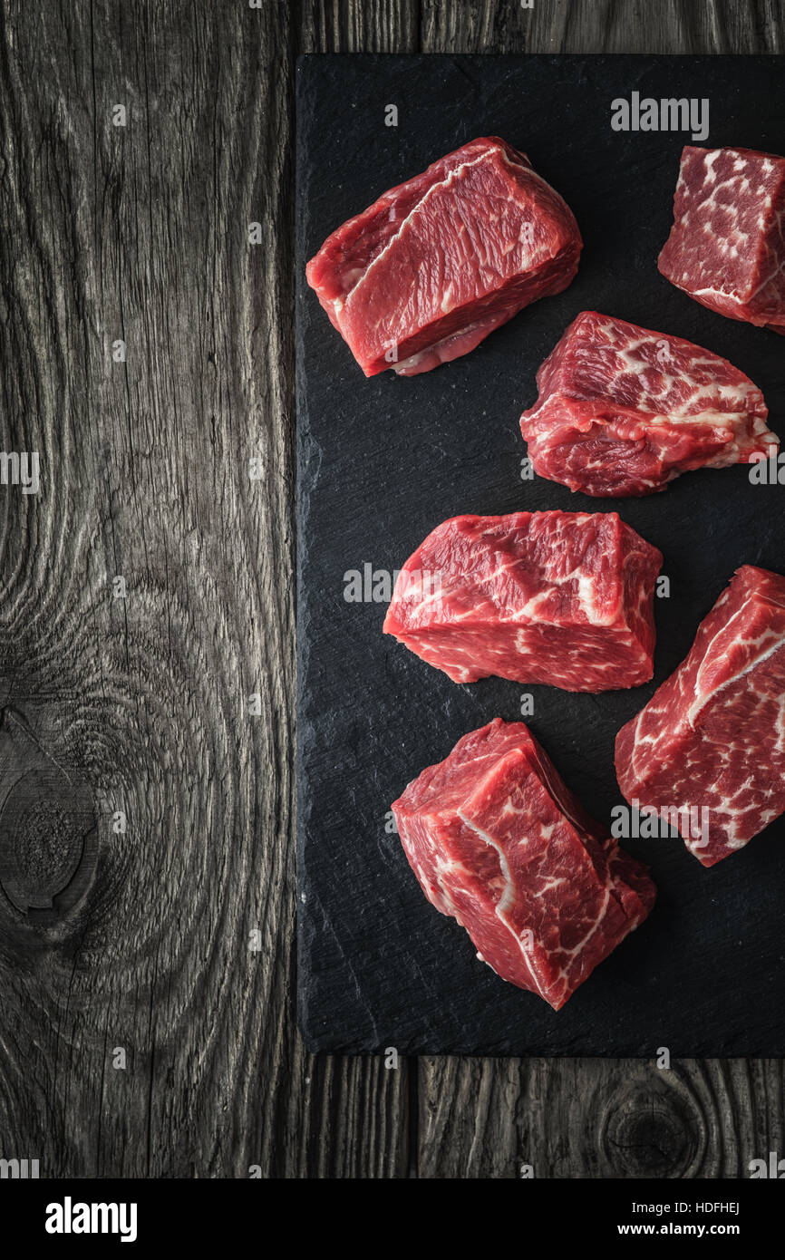 Roh Angus-Rindfleisch-Scheiben auf dem schwarzen Stein auf den Holztisch vertikale Stockfoto