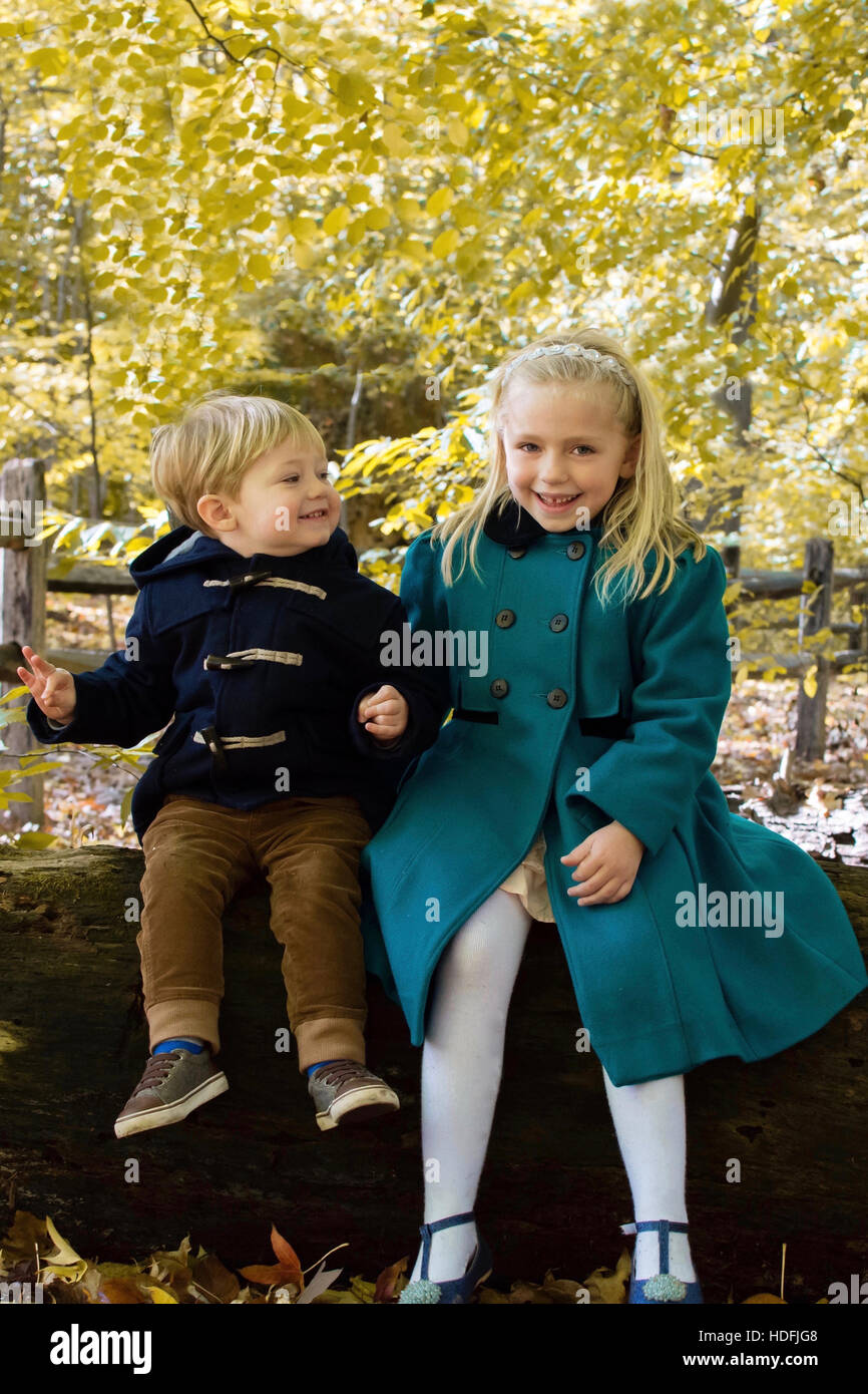 Bruder und Schwester Geschwister tragen Wintermäntel sitzen auf Log im Herbst fallen Saison im park Stockfoto