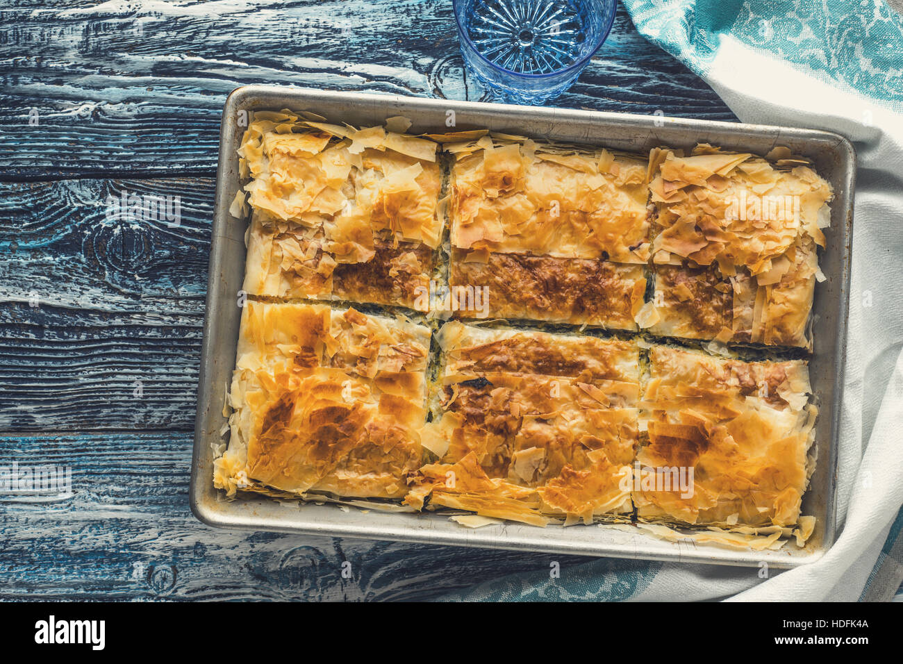 Griechischer Kuchen Spanakopita in der Metall-Pfanne auf der blauen hölzernen Tischplatte Ansicht Stockfoto