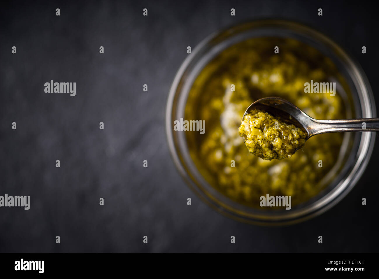 Pesto-Soße in der Metalllöffel mit unscharfen Glas Draufsicht Stockfoto