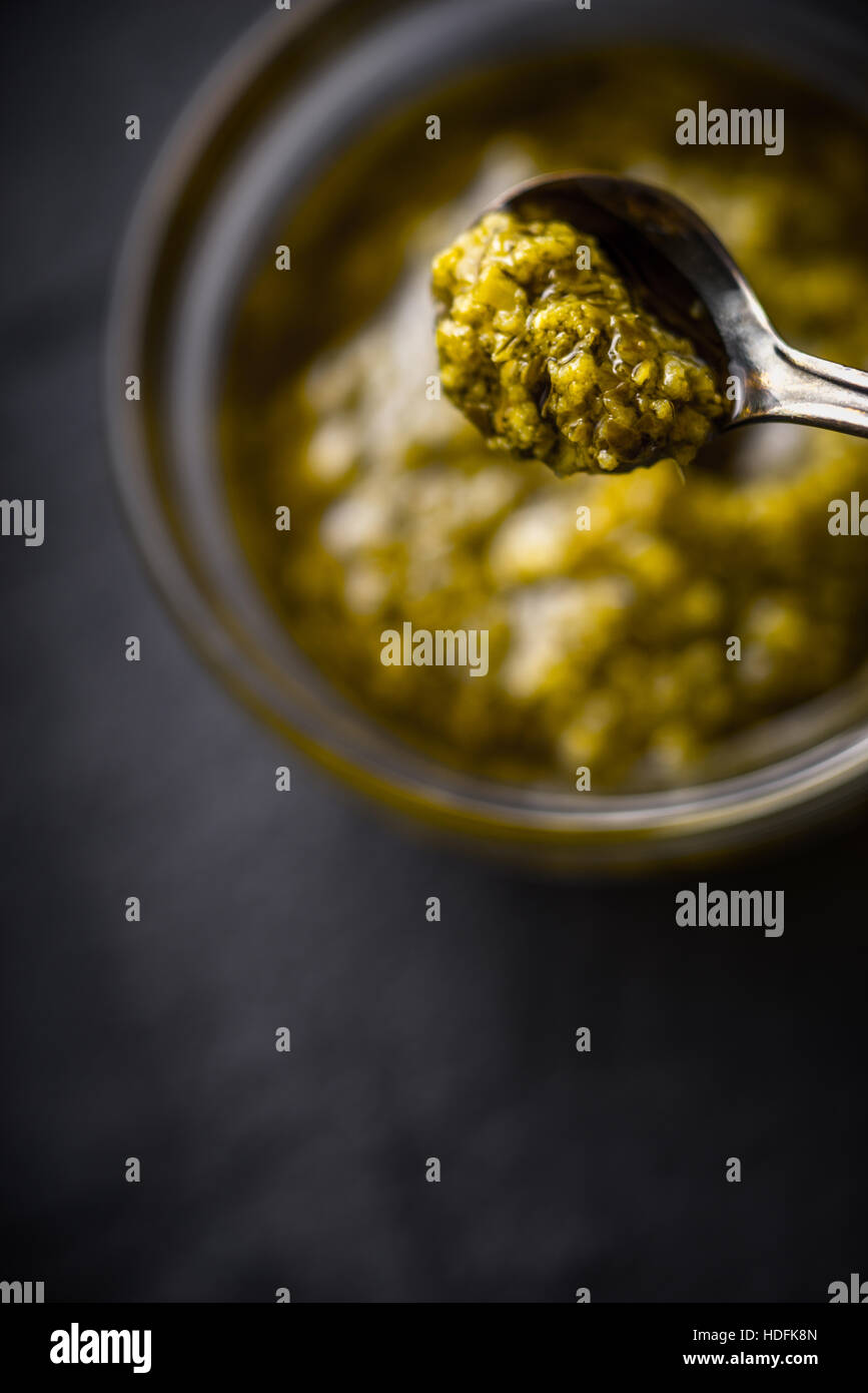 Pesto-Soße in Metalllöffel mit unscharfen Glas vertikal Stockfoto