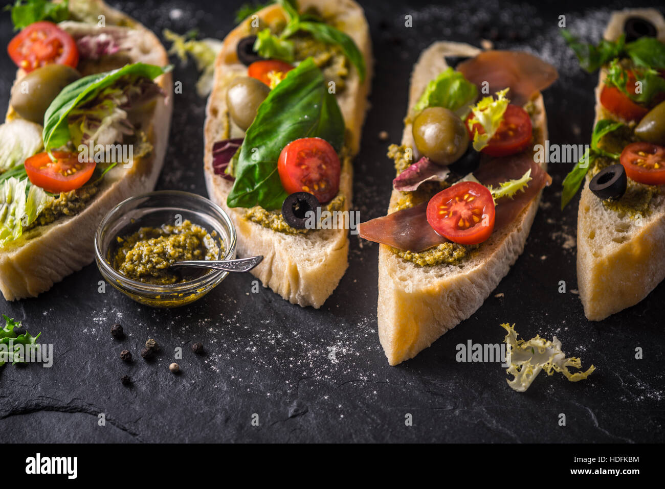 Scheiben vom Ciabatta mit Oliven, Tomaten und Basilikum auf dem schwarzen Stein Tisch Stockfoto