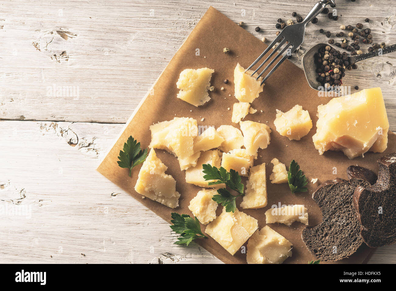 In Scheiben Parmesan mit Brot, Petersilie und Pfeffer auf dem Pergament auf der weißen hölzernen Tischplatte-Ansicht Stockfoto