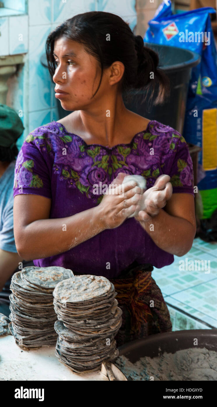 Eine junge Maya-Frau in traditioneller Kleidung macht blauem Mais Tortillas auf dem Markt von Santiago Atitlan, Guatemala. Sie ist sie zwischen den Händen streichelte. Stockfoto