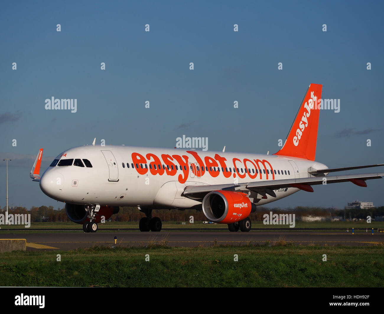 Das Flugzeug G-EZOA wird am Flughafen Schiphol, Niederlande, auf dem Weg zur Start- und Landebahn 36L. Das Bild zeigt die Vorbereitung des Flugzeugs auf den Start und zeigt sein detailliertes Design und die geschäftige Flughafenumgebung. Schiphol ist einer der verkehrsreichsten Flughäfen Europas, bekannt für seinen effizienten Betrieb und sein hohes Verkehrsaufkommen. Stockfoto