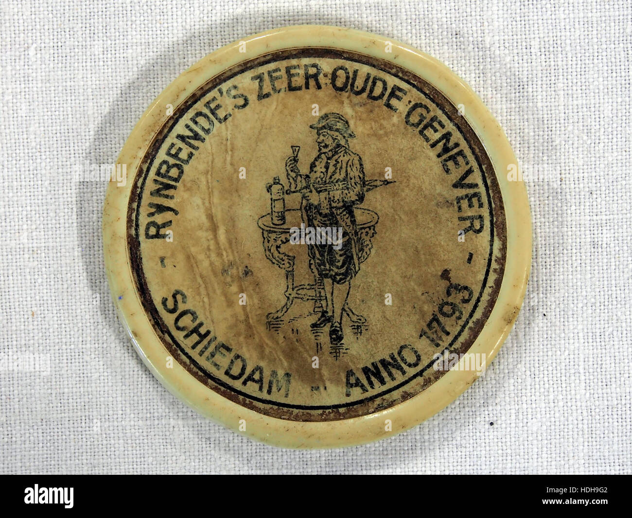 Der Rynbendes zeer Oude Genever reklamespiegeltje ist ein antiker Werbespiegel, der den alten niederländischen Genever-Geist fördert. Es spiegelt das Marketing des frühen 20. Jahrhunderts wider, wobei das Branding an Kekse, Zigaretten und Genever-Lagerung gebunden ist. Stockfoto